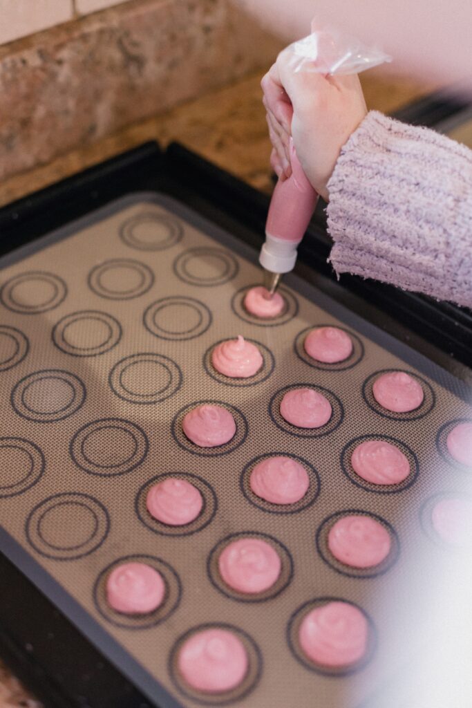 Someone piping pink batter onto a tray